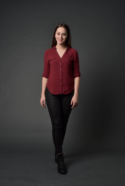 full length portrait of brunette girl wearing  red shirt and leather pants. standing pose , on grey studio background. - Fotoğraf, Görsel