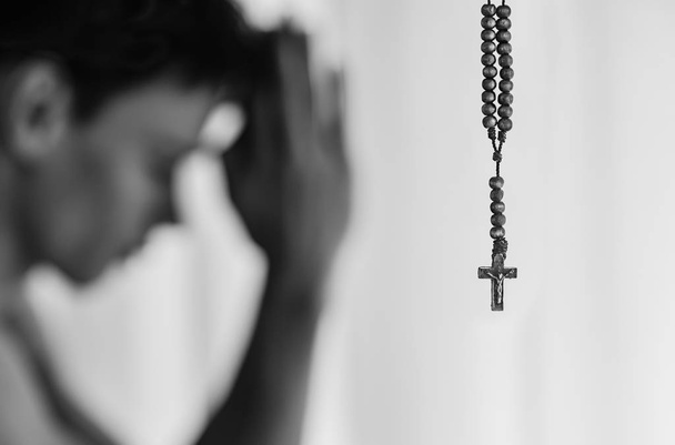 A cross hanging with rosary beads and a religious man praying in the back. - Photo, Image
