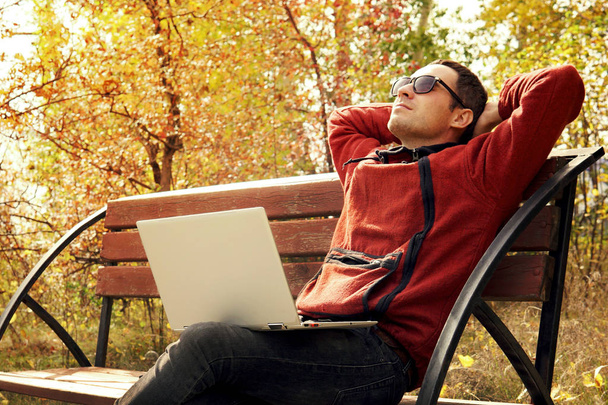 Hombre maduro feliz usando el ordenador portátil mientras está sentado en la cerca contra el lago. Joven él especialista toman un descanso del trabajo. Trabajo remoto al aire libre. El estudiante está siendo reescrito en Internet
 - Foto, imagen
