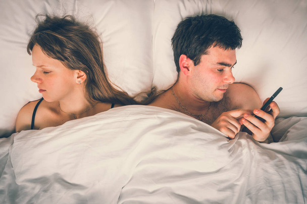 Młody człowiek za pomocą telefonu komórkowego, podczas gdy jego żona snu w nocy - bezsenność i oszukiwanie koncepcja - styl retro - Zdjęcie, obraz