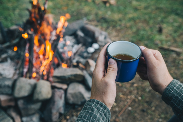 first point of view. man drinking tea in metal cup near camp fire. hiking - Фото, зображення