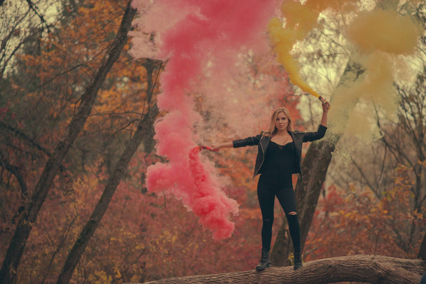 Girl with red and yellow smoke bombs in autumn - Фото, зображення