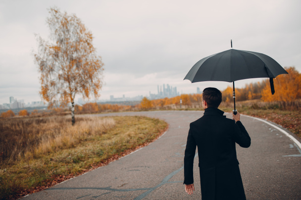 Młody człowiek w czarnym płaszczu, spacery w deszczu z parasolem - Zdjęcie, obraz