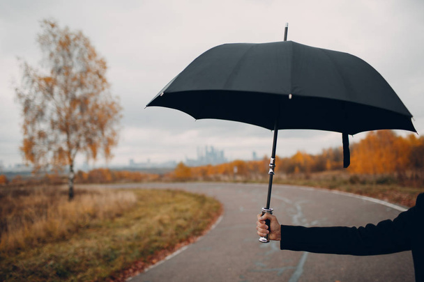 Young man in black holds umbrella in hand close up - Foto, Bild