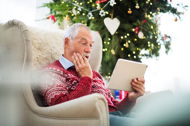 A senior man at home at Christmas time, using tablet. - Valokuva, kuva