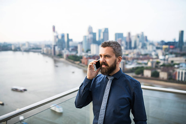 A portrait of businessman with smartphone standing against London view panorama. - Фото, зображення