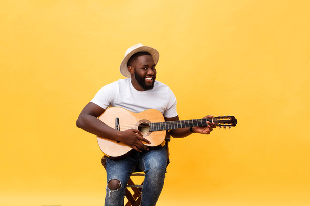 Handsome african american retro styled guitarist playing acoustic guitar isolated on yellow background. - Foto, afbeelding