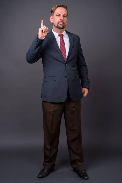 Blonder bärtiger Geschäftsmann mit Spitzbart vor grauem Hintergrund - Foto, Bild