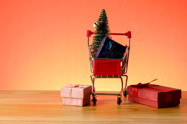 CONCEPTUAL DE AÑO NUEVO con carrito de compras, cajas de regalo y árbol de Navidad en una mesa de madera
. - Foto, imagen