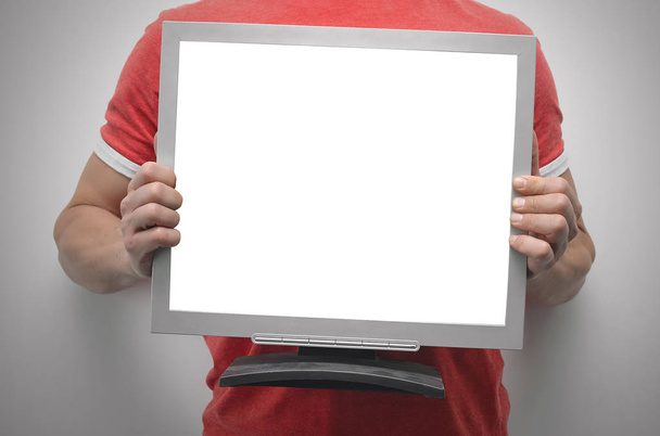 Man is holding a computer monitor with blank screen in front of him isolated on gray background. - Photo, Image