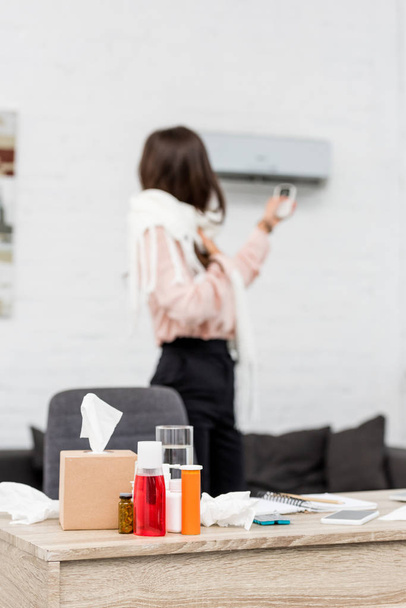 sick young woman pointing at air conditioner with remote control with medicines on foreground - Photo, Image