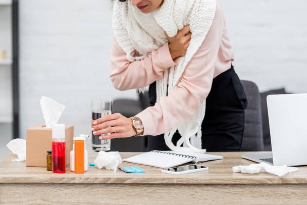 cropped shot of suffering sick young businesswoman taking glass of water from desk with meds - 写真・画像