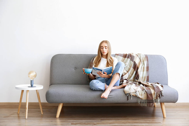 Young beautiful woman wearing white t-shirt on grey textile sofa at home. Attractive slim female in domestic situation, resting on couch in her lofty apartment. Background, copy space, close up. - Fotografie, Obrázek