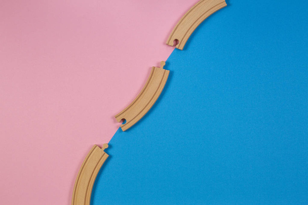 Wooden toy train rails pieces on blue and pink color background - Fotó, kép