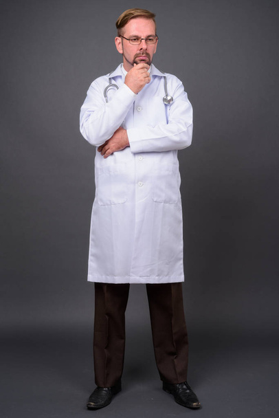 Ξανθός γενειοφόρος γιατρός άνθρωπος με μουσάκι σε γκρι φόντο - Φωτογραφία, εικόνα