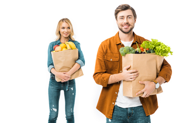 happy young man holding shopping bag with products while his girlfriend standing behind isolated on white - Fotó, kép