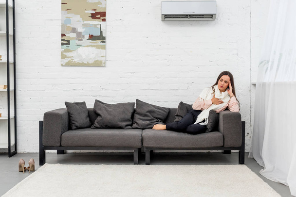 mujer joven enferma acostada en el sofá bajo condiciones de aire en casa
 - Foto, Imagen