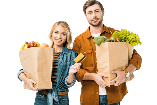 portrait of young woman showing credit card while her boyfriend standing near with shopping bags full of products isolated on white - Фото, изображение