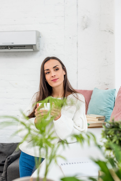 beautiful young woman holding cup of coffee while leaning on windowsill - Photo, Image