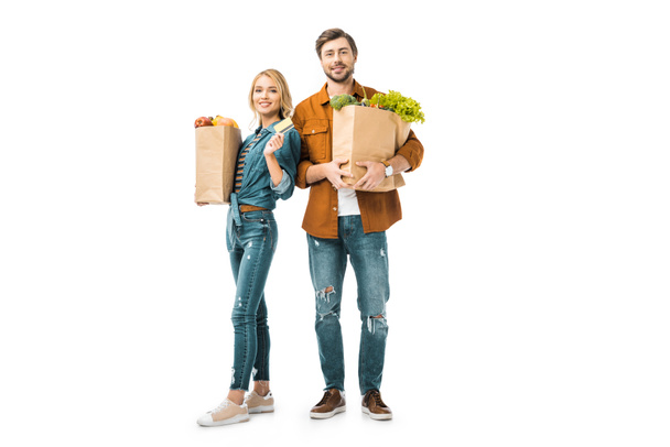 attractive cheerful girl showing credit card while her boyfriend standing near with shopping bags full of products isolated on white - Photo, Image