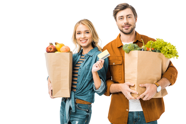 smiling beautiful girl showing credit card while her boyfriend standing near with shopping bags full of products isolated on white - Photo, Image
