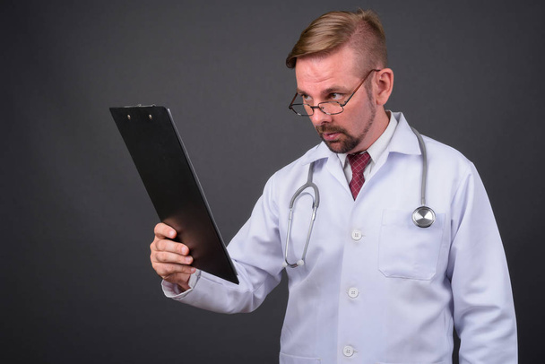 Ξανθός γενειοφόρος γιατρός άνθρωπος με μουσάκι σε γκρι φόντο - Φωτογραφία, εικόνα