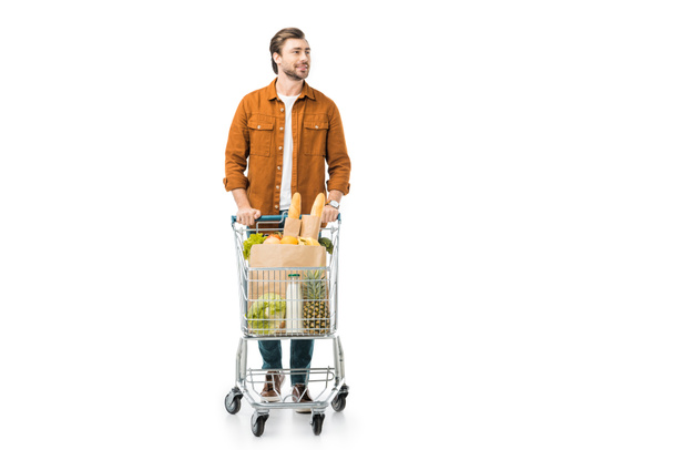 schöner Mann trägt Einkaufswagen mit Produkten in Papiertüten isoliert auf weiß - Foto, Bild