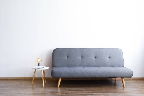 Minimalistische interieur concept. Grijs textiel sofa in ruime kamer van loft-stijl appartement met hout getextureerde gelamineerde bevloering. Background, kopiëren van ruimte, close-up. - Foto, afbeelding