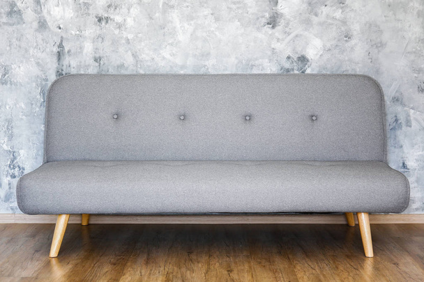 Concepto minimalista de diseño de interiores. Sofá textil gris en amplia habitación de estilo loft apartamento con suelos laminados con textura de madera. Fondo, espacio de copia, primer plano
. - Foto, Imagen