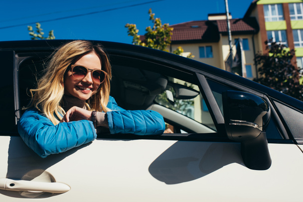 cheerful young woman in sunglasses leaning out car on street - Foto, Imagen