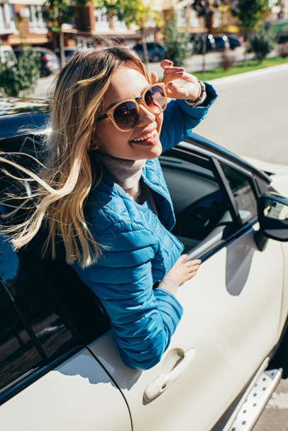 路上の車をもたれてサングラスで陽気な若い女性 - 写真・画像