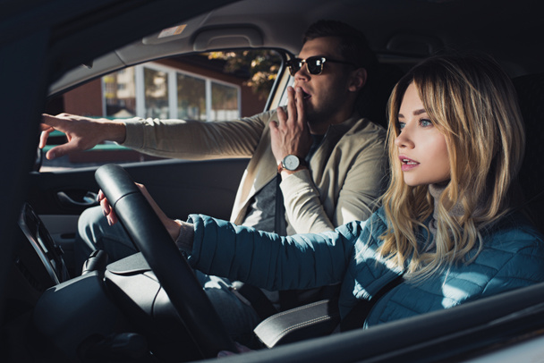 shocked man showing direction to girlfriend on drivers seat in car - Φωτογραφία, εικόνα