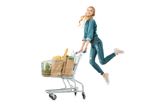 pozytywne, piękna dziewczyna, skoki w pobliżu shopping cart wózek z produktów w worki papierowe na białym tle - Zdjęcie, obraz