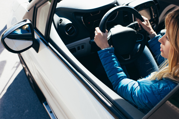 vista lateral de la mujer joven con las manos en el volante de conducción del coche
 - Foto, Imagen