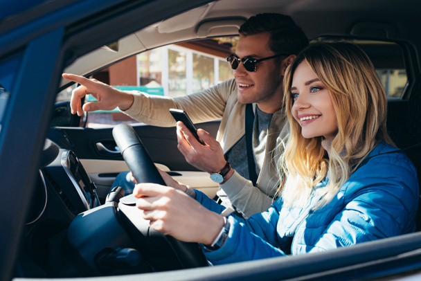 uomo sorridente con smartphone che mostra la direzione alla ragazza che guida auto
 - Foto, immagini