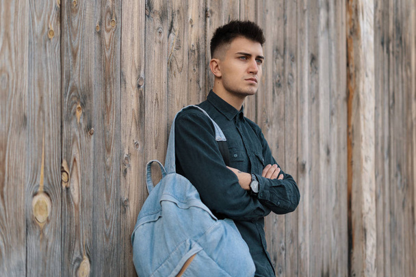 Young stylish student posing with a jean backpack on wooden background with copy space. - Photo, image