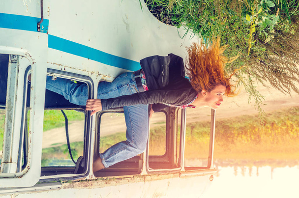 Menina jovem cabelo vermelho senta-se na borda da janela de um ônibus quebrado
 - Foto, Imagem