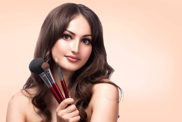 Closeup portrait of pretty woman with cosmetics brushes, pastel background - Photo, Image