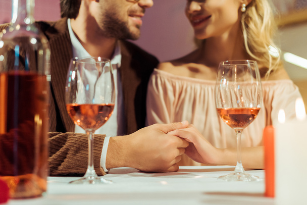 abgeschnittenes Bild eines Paares, das sich Händchen hält und sich mit Weingläsern am Tisch im Restaurant verabredet  - Foto, Bild