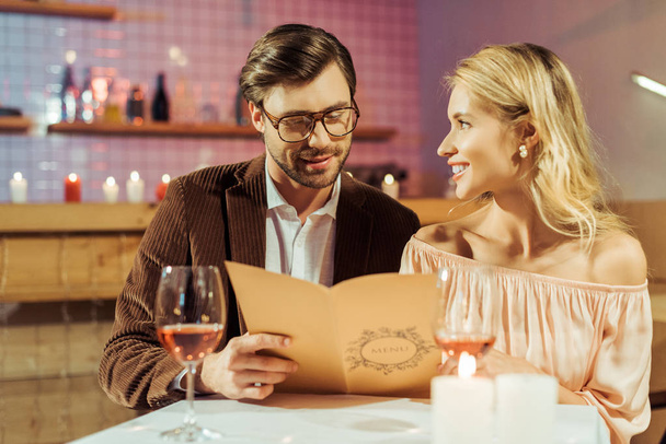 glückliches junges Paar beim Blick auf die Speisekarte während des romantischen Abendessens im Restaurant  - Foto, Bild