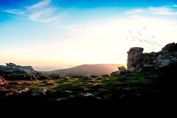 A view over Dartmoor from a granite tor, in the early morning light with a flock of birds flying over. - Photo, Image