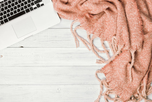 Home office desktop with a laptop, cozy warm pink plaid. Wooden white table, flat lay. Winter or autumn background, top view - Photo, Image