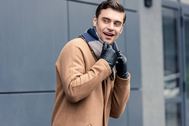 handsome smiling man in coat and scarf looking away on street - Foto, imagen