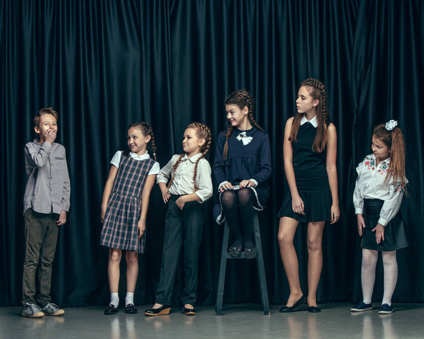 Cute stylish children on dark studio background. The beautiful teen girls and boy standing together - Zdjęcie, obraz