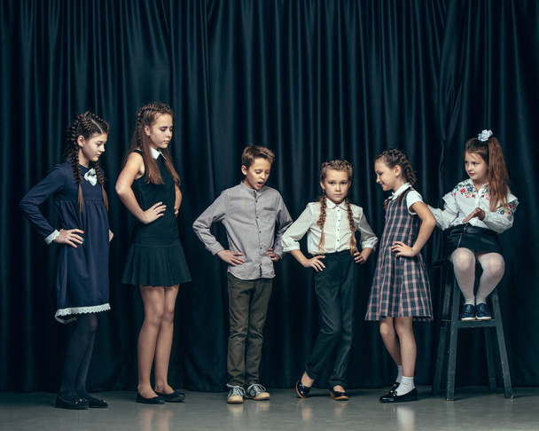 Cute stylish children on dark studio background. The beautiful teen girls and boy standing together - Foto, Imagem