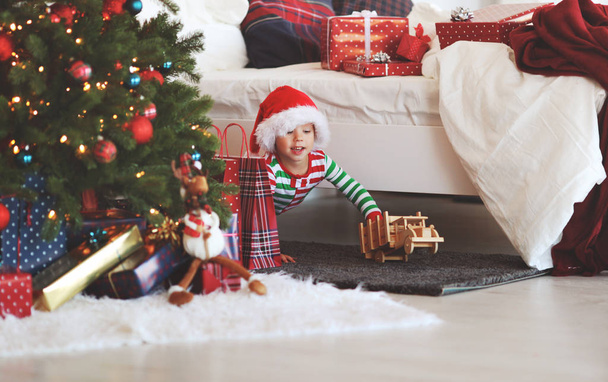 szczęśliwy chłopca w piżamie z prezenty na Boże Narodzenie rano w pobliżu tre Boże Narodzenie - Zdjęcie, obraz