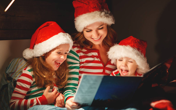 Wesołych Świąt Bożego Narodzenia! Rodzina Matka czyta dzieciom książki przed łóżko łóżku - Zdjęcie, obraz