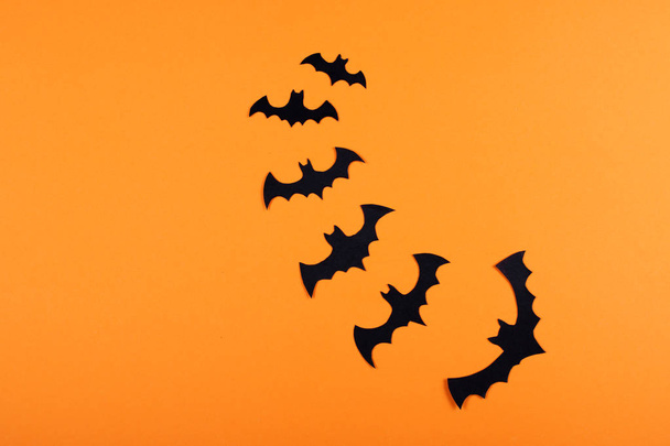 A flock of black paper bats on the orange wall. Halloween concept. - Фото, изображение