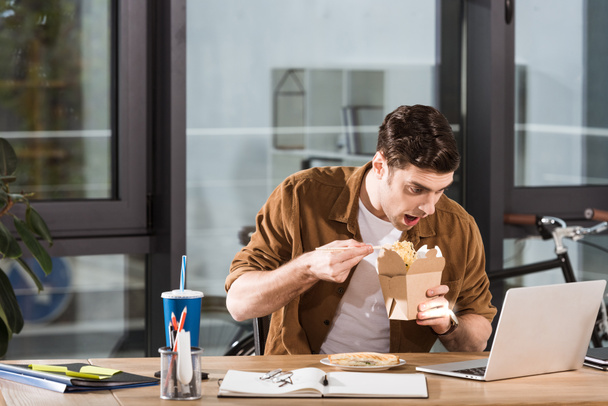 голодний бізнесмен, що їсть забирає локшину з коробки в офісі
 - Фото, зображення