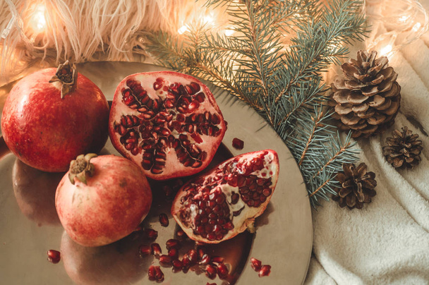 Acogedora mañana de invierno en casa con frutas. Granada en una composición invernal, árboles de Navidad, conos en un frasco en el fondo
 - Foto, Imagen